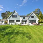 Modern family home exterior showcasing a large lawn and garden under a clear blue sky.