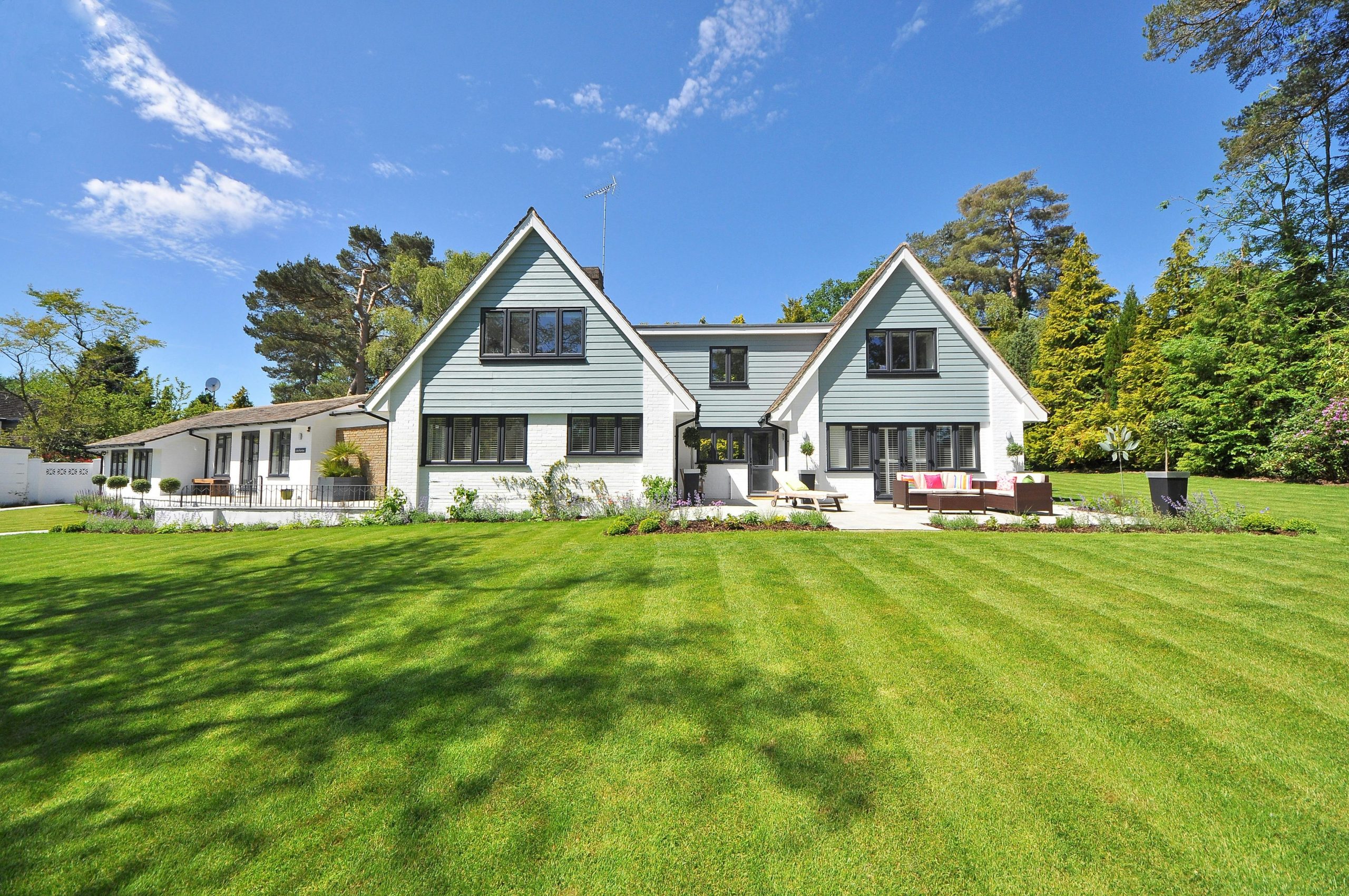 Modern family home exterior showcasing a large lawn and garden under a clear blue sky.