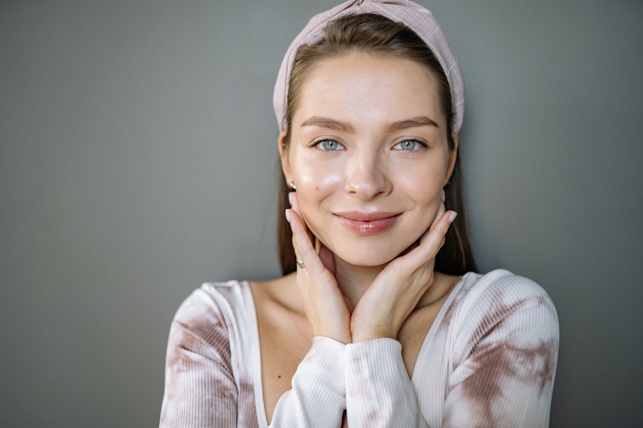 Portrait of a smiling woman with healthy skin wearing a headband on a gray background.