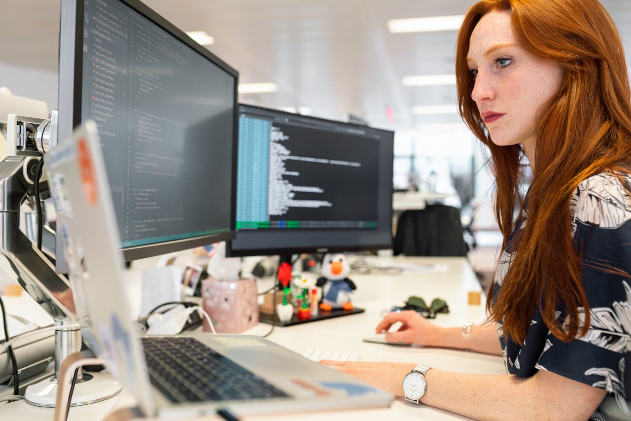 services-01 A focused female software engineer coding on dual monitors in a modern office.