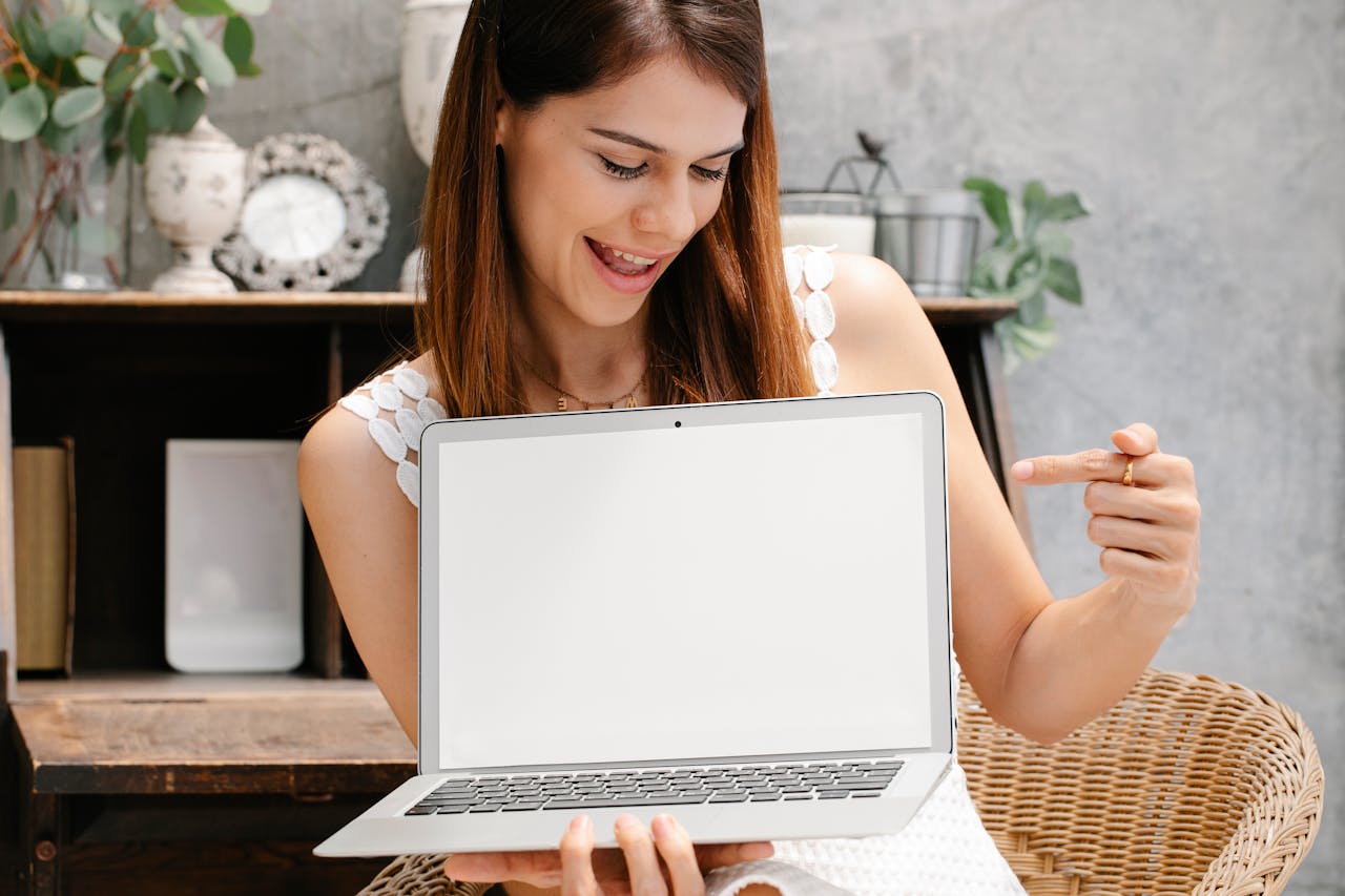 about-02 Young woman holding and pointing at a laptop with a blank screen, ideal for mockups.